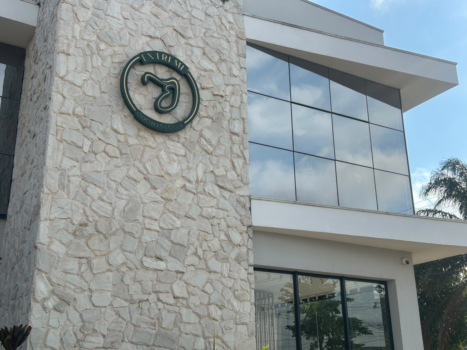 Fachada da Extreme Odontologia em Sinop, com parede de pedra clara, placa verde com o logo e janelas de vidro