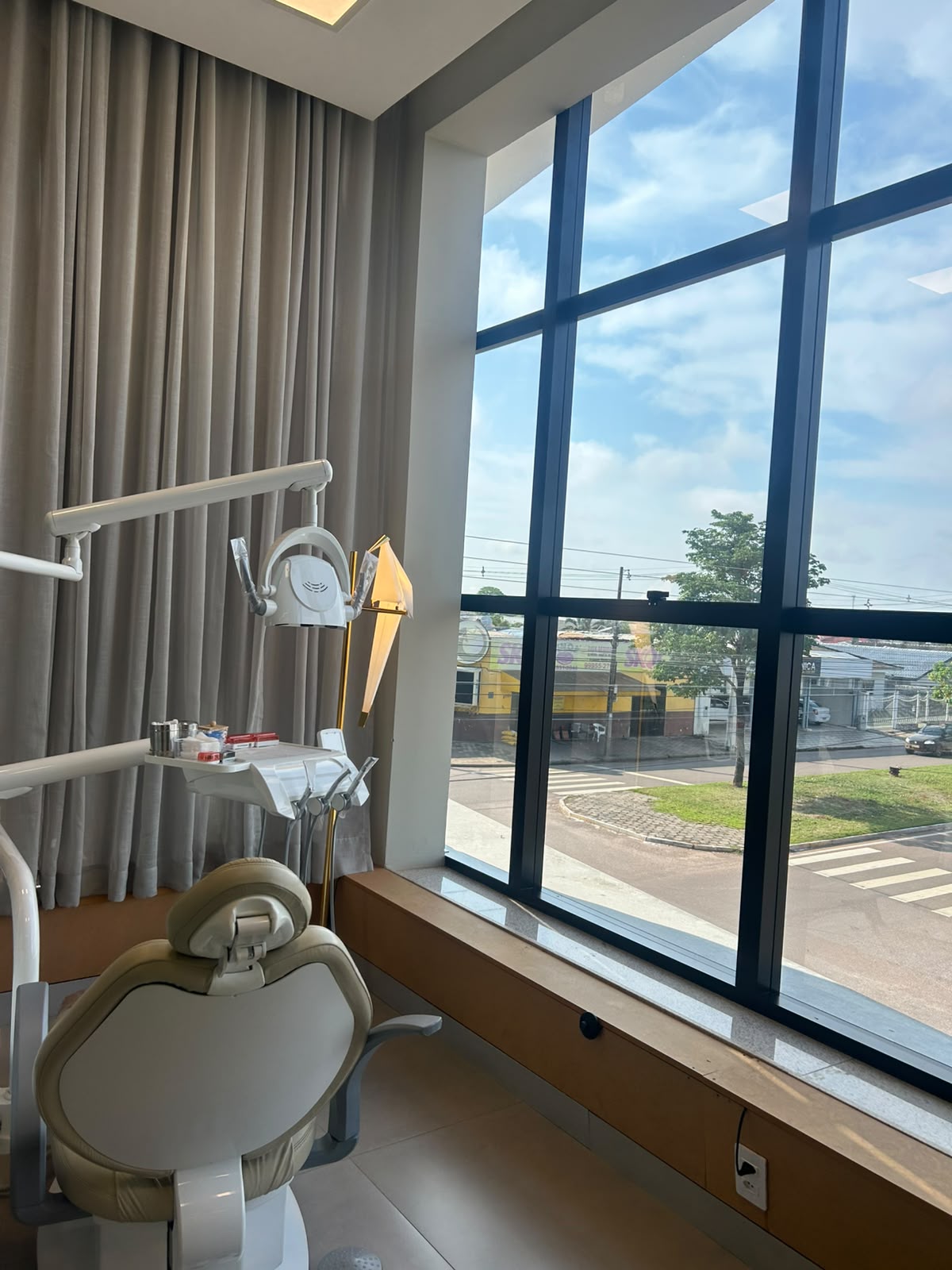 Sala clínica com cadeira odontológica clara ao lado de grandes janelas com vista para a cidade de Sinop