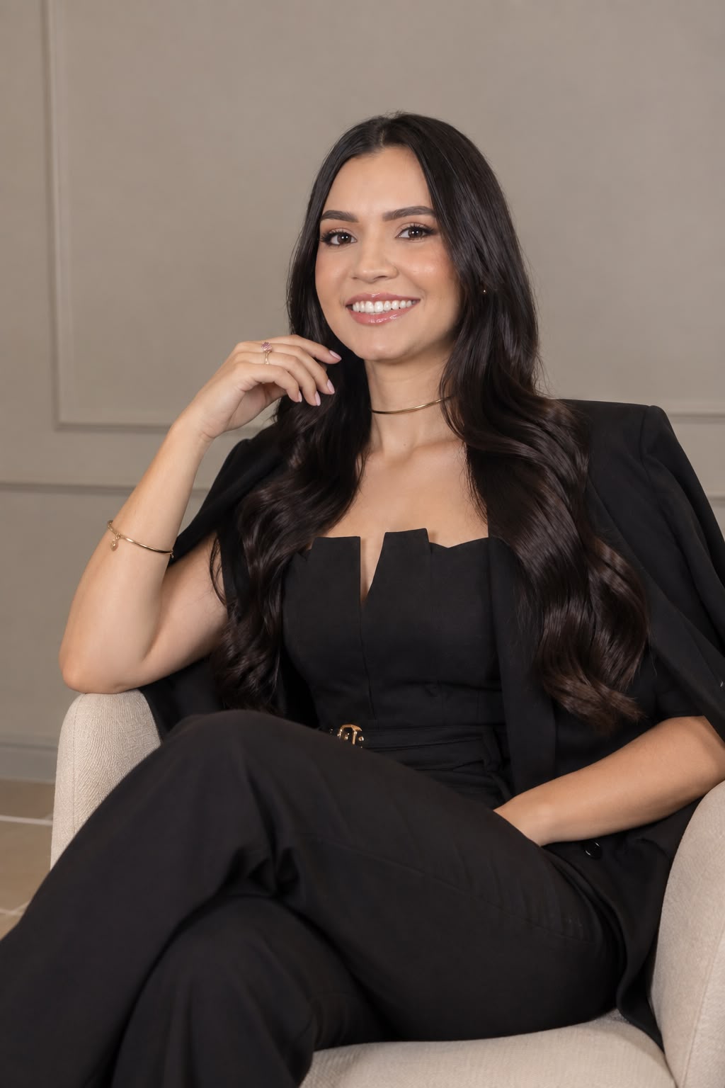 Retrato profissional da Dra. Katia Marcilio sorrindo, sentada em uma poltrona clara, vestindo roupa preta